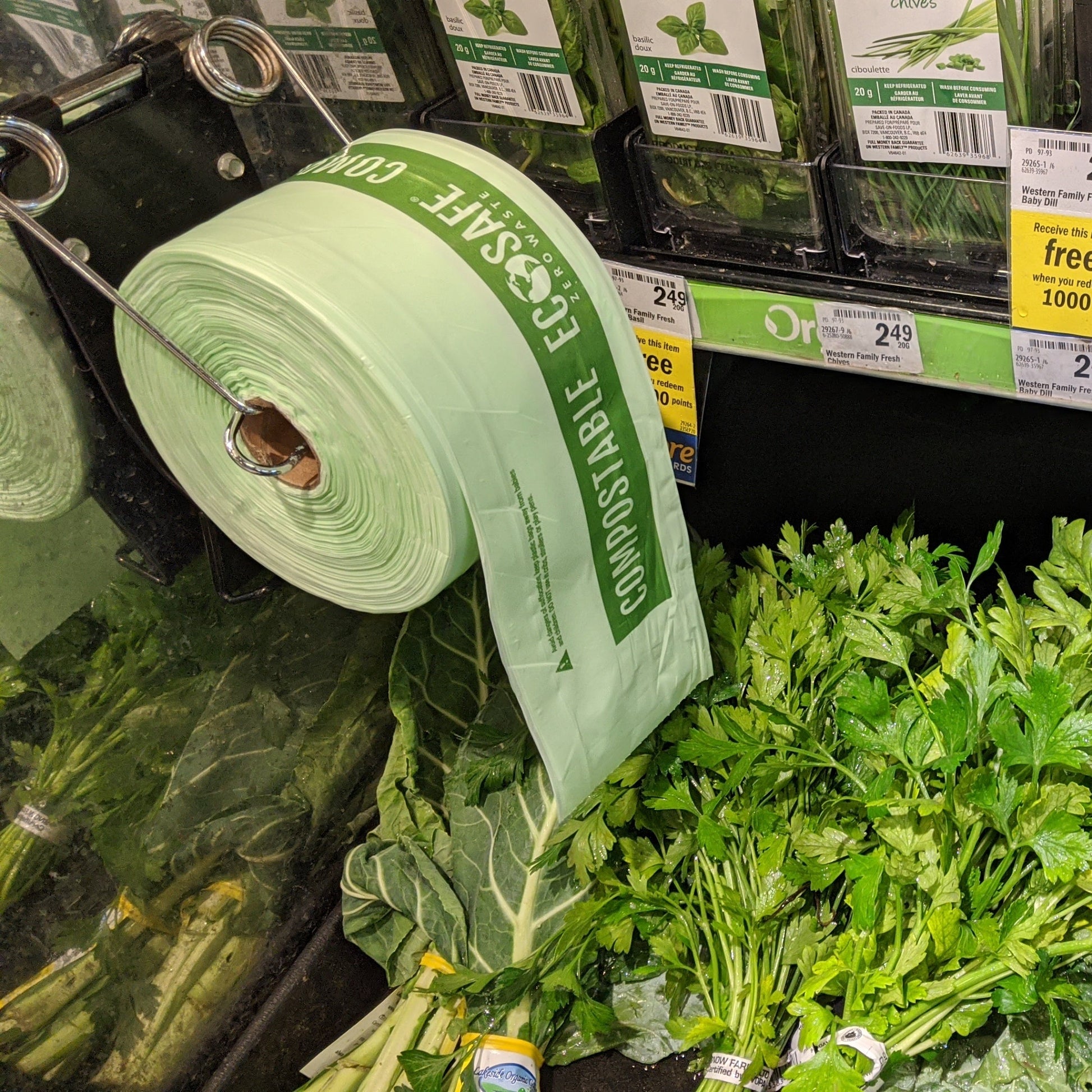 Grocery store produce section with green vegetables and a roll of EcoSafe Produce Bags