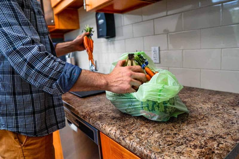 Person taking out vegetables from compostable checkout bag on kitchen counter